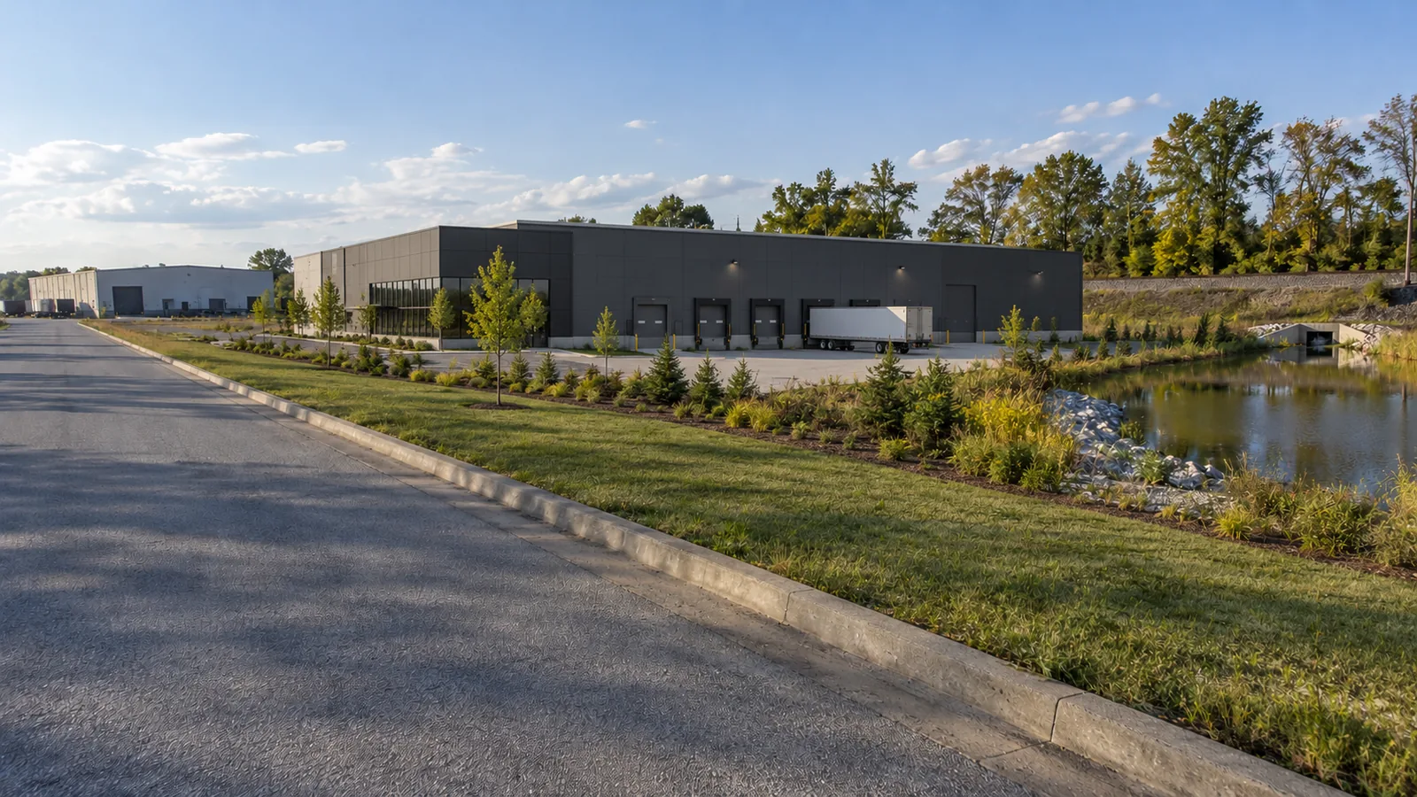 The same street frame with a low distribution building behind a landscaped pond edge